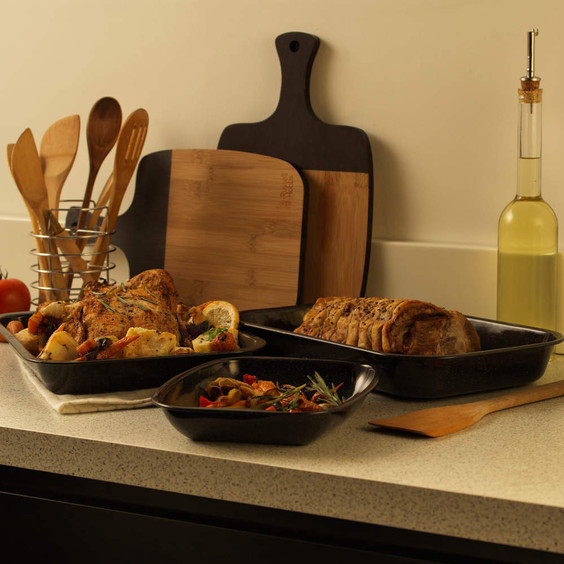 Set of black roasting trays with cooked chicken and pastry on kitchen counter
