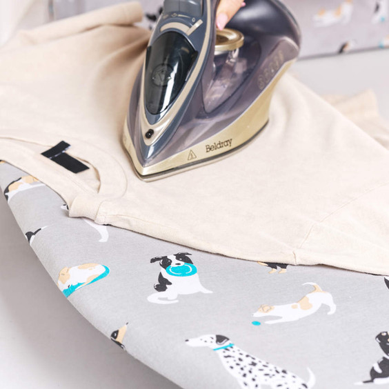 Steam iron on beige shirt, ironing board with grey dog print cover