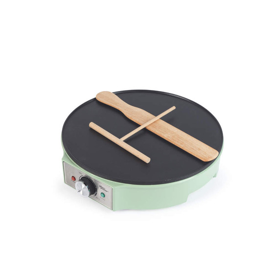 Green electric crepe maker with wooden spatula and spreader on hot plate