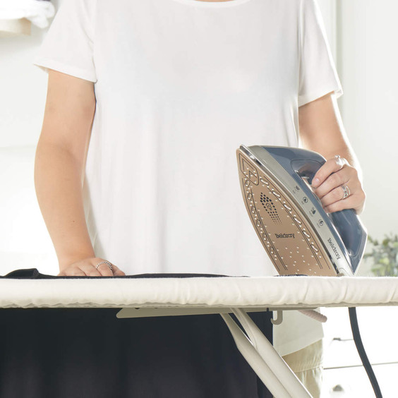 Person ironing black garment with gold and navy Beldray steam iron on board