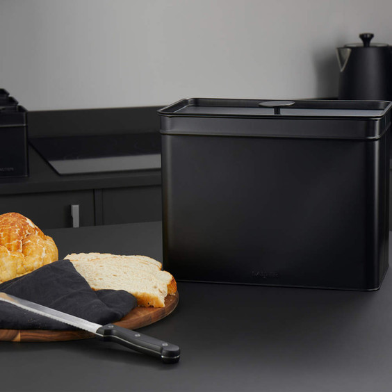 Black metal bread bin on kitchen worktop, next to sliced loaf and bread knife.