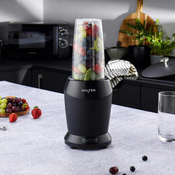 Black personal blender with clear cup filled with fruit, shown on kitchen counter