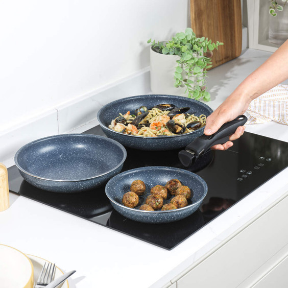 Set of three blue speckled frying pans with detachable handle, shown cooking on hob.