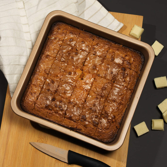 Tray of golden blondies with white chocolate chunks, cut into squares.