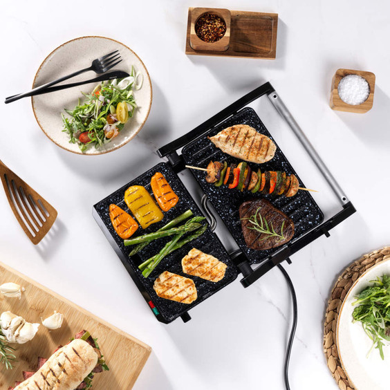 Tabletop electric grill cooking assorted meats and vegetables, shown in use.