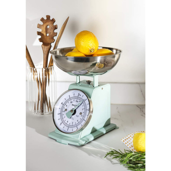 Mint green mechanical kitchen scale with lemons in bowl, shown on countertop.
