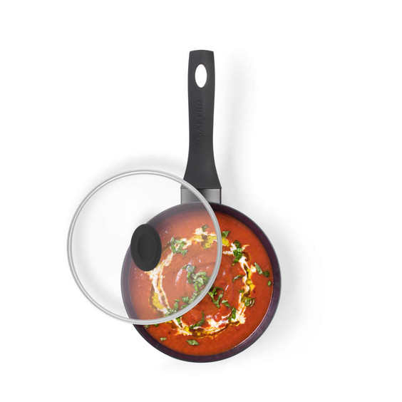 Black non-stick saucepan with lid, top view, filled with tomato soup and herbs