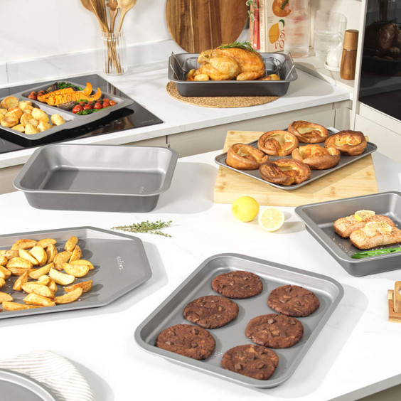 Non-stick grey bakeware set with roast chicken, vegetables, Yorkshires and cookies displayed.