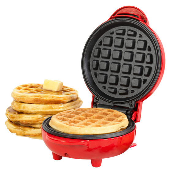Red waffle maker open, showing cooked waffle inside with stack of waffles and butter beside