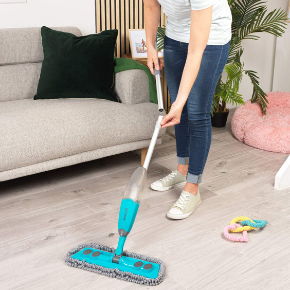 Person using blue spray mop to clean wood floor in modern living room