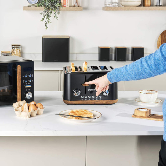Black four-slice toaster in use on kitchen worktop, with toast, eggs and coffee nearby