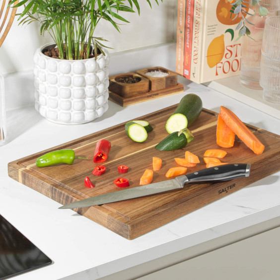 Salter chef’s knife on wooden chopping board with sliced carrot, courgette, and peppers.