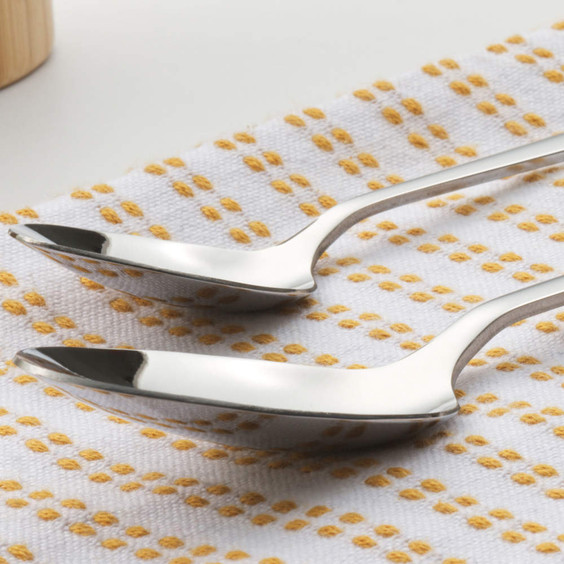 Pair of stainless steel spoons on white and yellow textured tea towel