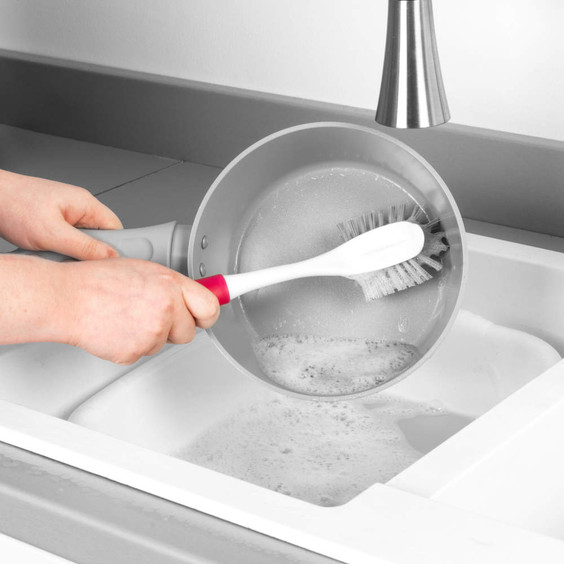 Washing-up brush with pink handle cleaning saucepan in kitchen sink