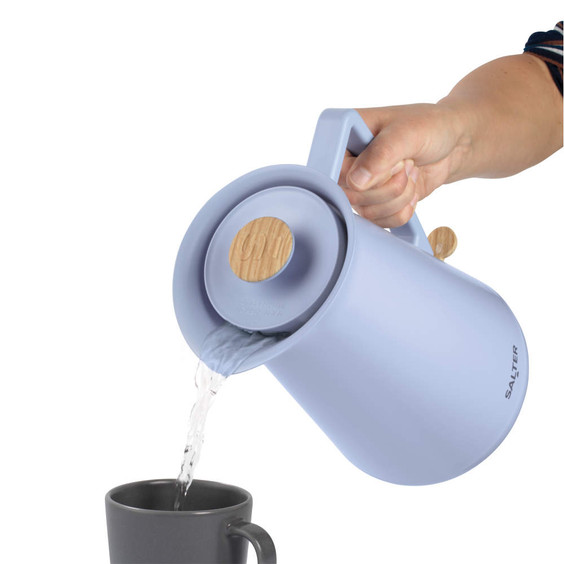 Blue electric kettle with wood accents pouring hot water into a black mug, shown in use.