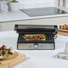 Stainless steel panini press with toasted sandwich, shown open on a kitchen counter.