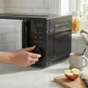 Hand adjusting black microwave timer on kitchen counter, next to mug and apple