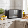 Black microwave oven on kitchen worktop near lemons, bread and olive oil