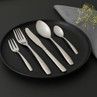 Five-piece silver cutlery set on black plate, includes knife, forks and spoons.