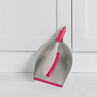 Grey dustpan and pink-handled brush set shown leaning against white kitchen cupboard.