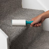 Lint roller with blue handle used on grey carpeted stairs