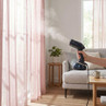 Handheld garment steamer releasing steam in living room, shown against pink curtains.