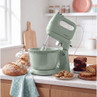 Green stand mixer with bowl on kitchen counter, surrounded by fresh baked goods