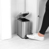 Silver pedal bin in bathroom, lid open, foot pressing pedal