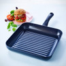 Black square non-stick grill pan next to veggie burger on plate, shown for product listing