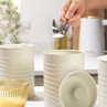 Set of cream kitchen canisters for coffee, sugar, and tea on counter, hand adding sugar