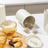 Cream kitchen canister set for tea, coffee and sugar, with amber cups and cake on worktop
