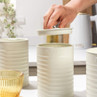 Cream kitchen canisters for sugar, coffee, and tea on worktop, hand opening sugar jar.