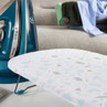 Patterned ironing board cover beside blue steam iron