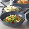 Non-stick frying pans with assorted cooked vegetables and roast chicken, kitchen setting