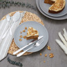 Three-piece silver cutlery set on grey plate with carrot cake slice and walnuts.