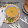 Bowl of creamy vegetable soup garnished with parsley, served with brown seeded bread.