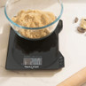 Black digital kitchen scale showing 200g in use with a glass bowl of brown sugar
