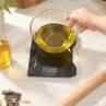 Electronic kitchen scale weighing glass bowl with oil, shown on countertop.