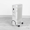 White oil-filled radiator heater with control dial on wheels, shown on light wood floor