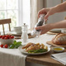 Clear pepper grinder seasoning chicken and vegetables on dining table