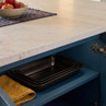 Set of three black roasting trays on blue kitchen shelf, shown with folded yellow tea towel.
