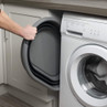 Front-loading washing machine with open grey door in fitted kitchen