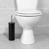 Black toilet brush and holder beside white toilet on grey tiled floor