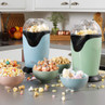 Blue and green popcorn makers on a kitchen counter with bowls of popcorn and sweets.