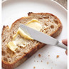 Knife spreading butter on wholemeal bread slice on white plate