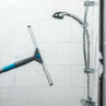 Shower squeegee cleaning glass shower screen with soap suds visible