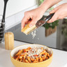 Grating cheese onto bowl of tomato pasta in kitchen