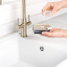 Filling a silver soap dispenser at a white kitchen sink
