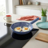 Blue non-stick frying pan with two fried eggs cooking on an induction hob