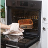 Gold round cake tin with baked cake being removed from oven using oven glove